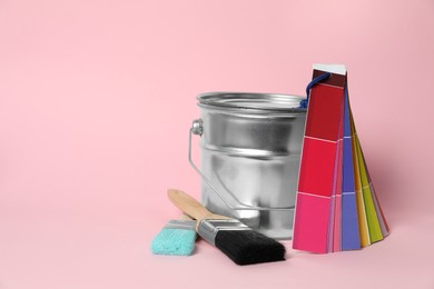 Photo of Can of paint, color palette samples and brushes on pink background. Space for text