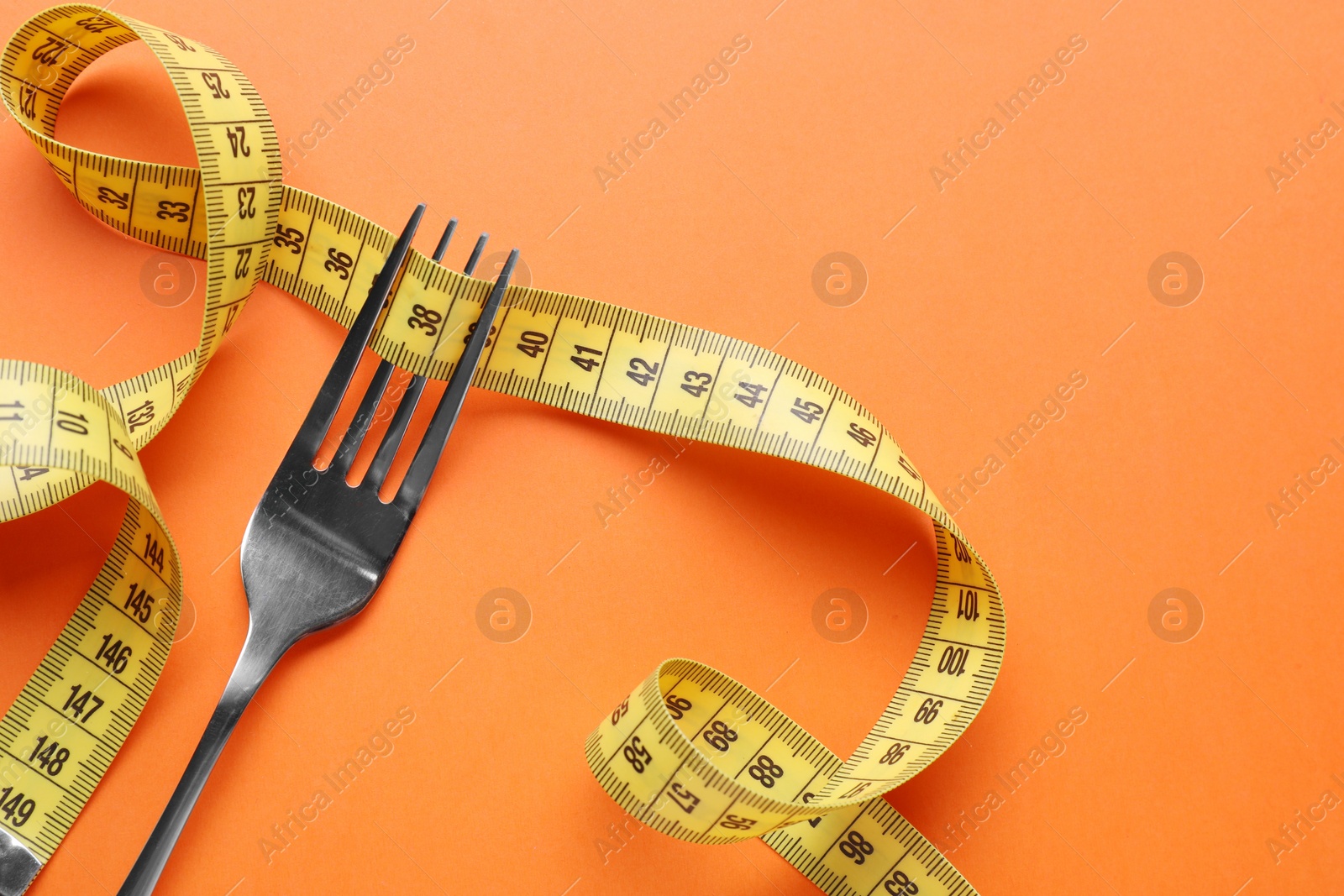 Photo of Fork with measuring tape on orange background, top view with space for text. Diet concept