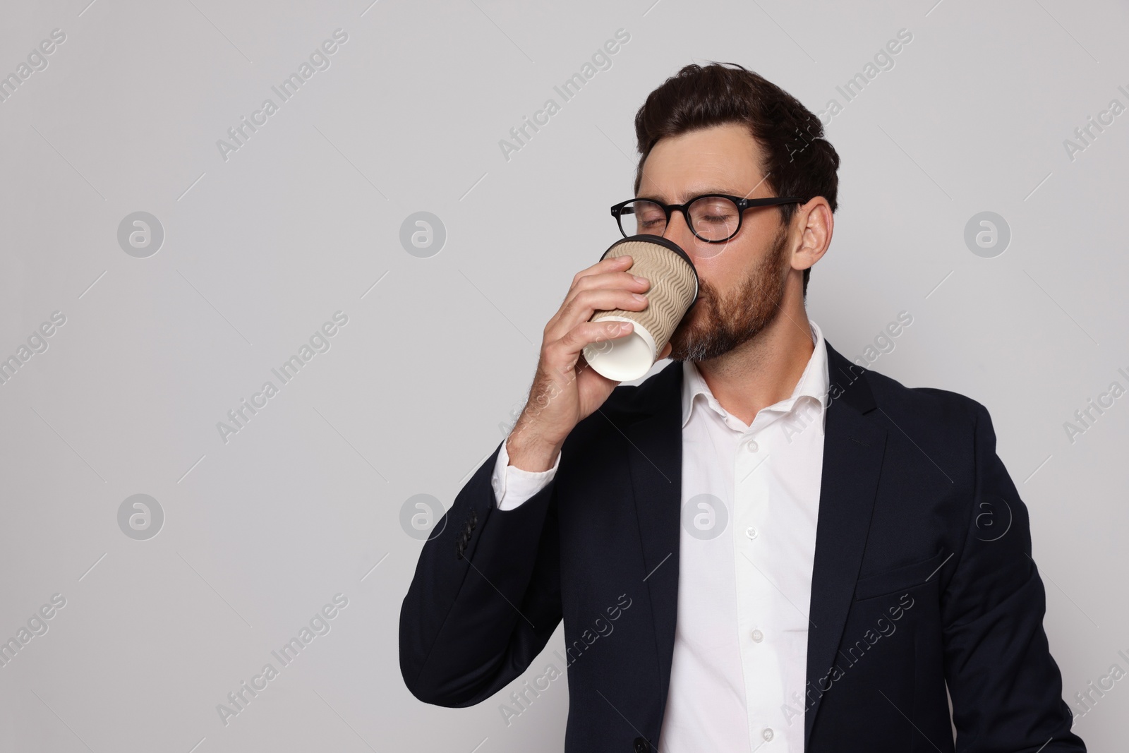 Photo of Handsome bearded man with glasses drinking from paper cup on light grey background. Space for text