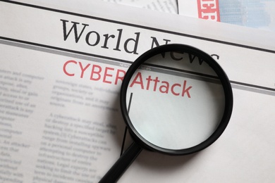 Newspaper with headline CYBER ATTACK and magnifying glass, top view