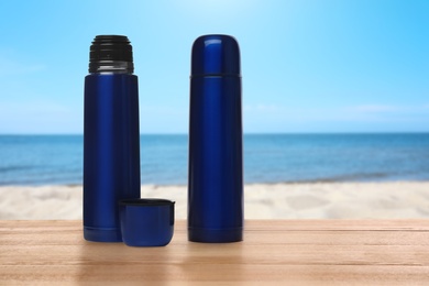 Image of Thermoses on wooden table near sea under blue sky