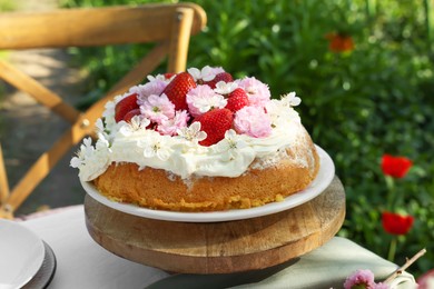 Photo of Delicious homemade cake decorated with fresh strawberries and spring flowers on table in garden