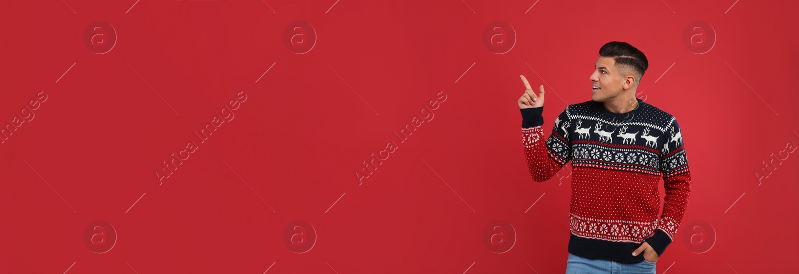Photo of Handsome man in Christmas sweater pointing on red background