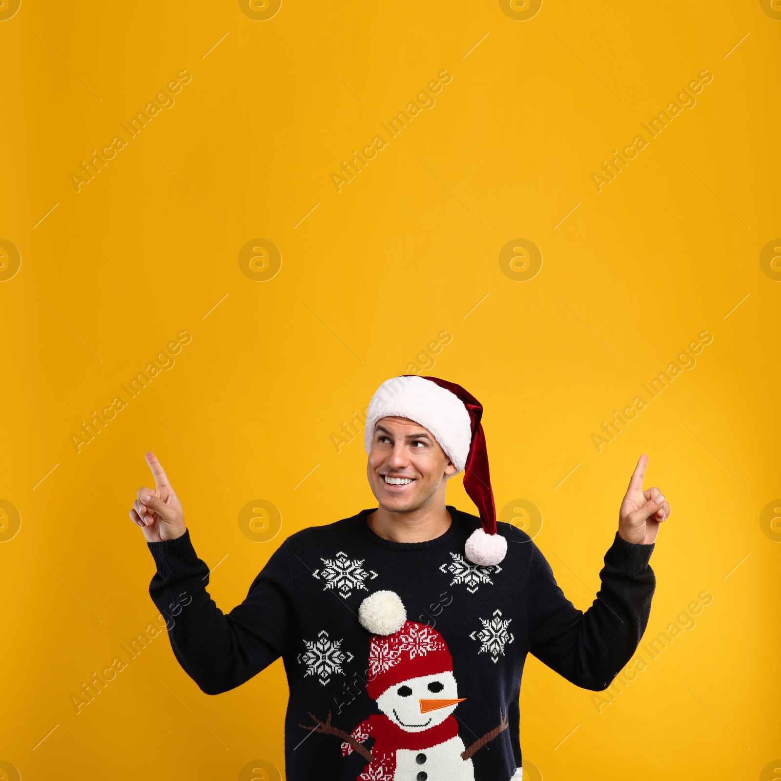 Photo of Happy man in Christmas sweater and Santa hat on yellow background