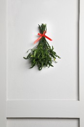 Photo of Mistletoe bunch with red bow hanging on light grey wall. Traditional Christmas decor