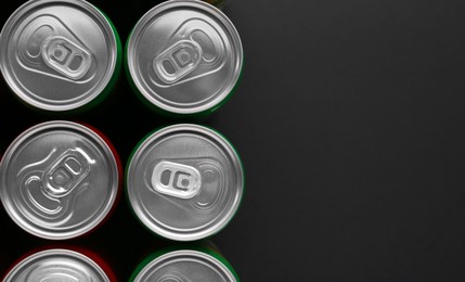 Photo of Energy drink in cans on black background, top view. Space for text