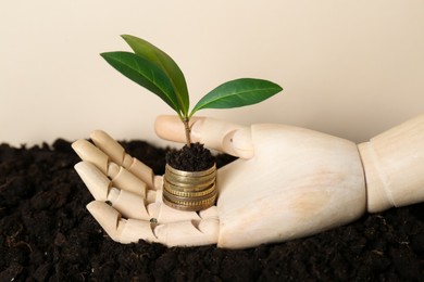 Mannequin hand with stack of coins and green plant on soil against beige background. Profit concept