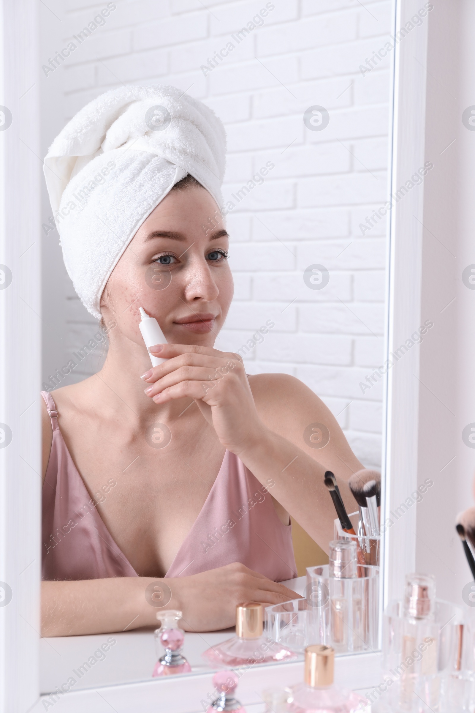 Photo of Woman with acne problem applying cream near mirror indoors