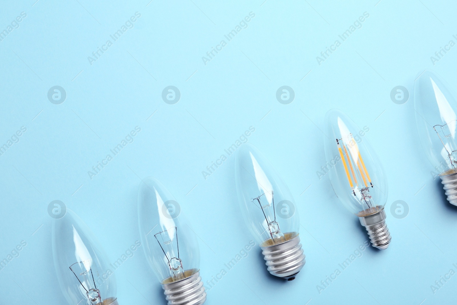 Photo of Vintage and modern lamp bulbs on light blue background, flat lay. Space for text