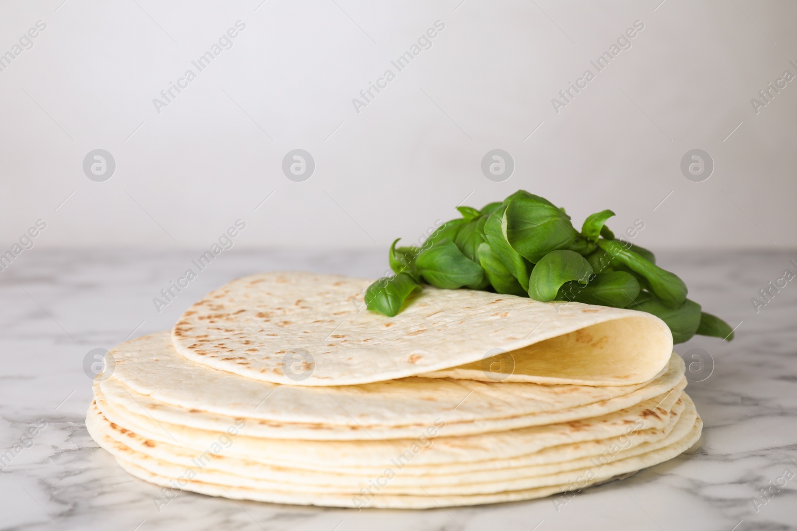 Photo of Stack of tasty tortillas with basil leaves on marble table. Space for text