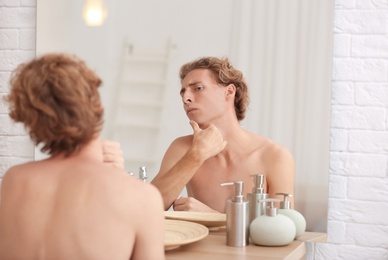 Young man looking in mirror after shaving at home