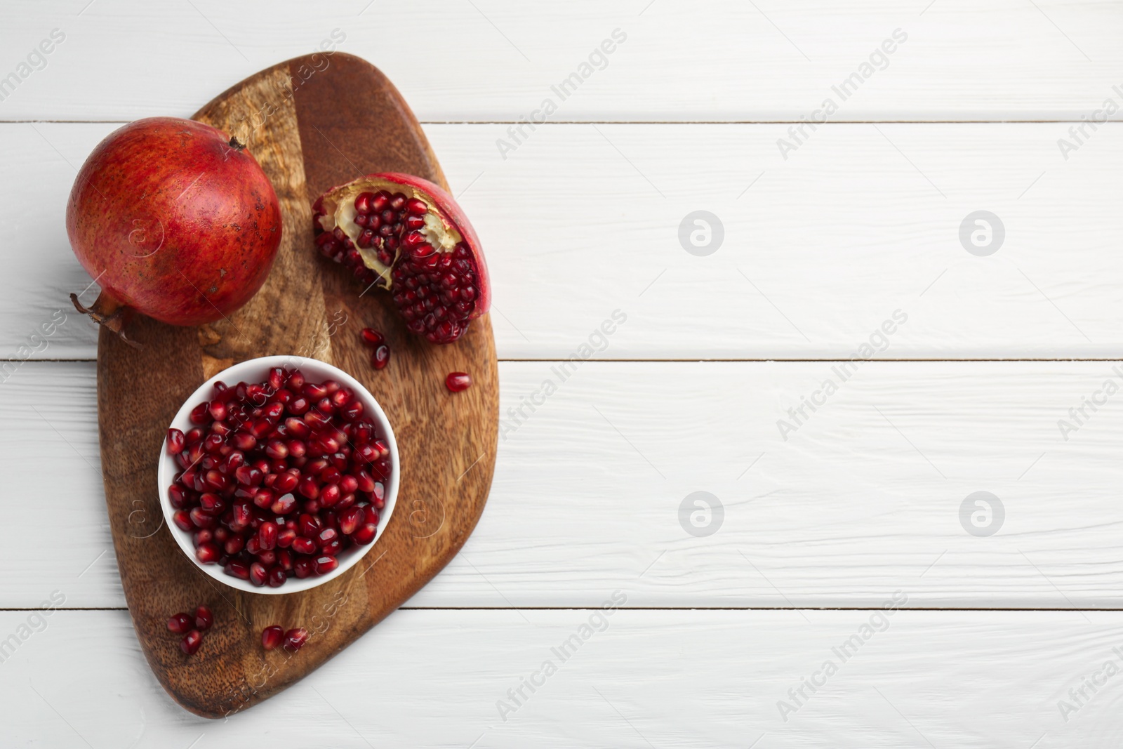 Photo of Ripe juicy pomegranate with grains on white wooden table, top view. Space for text