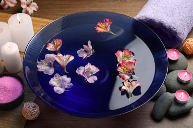 Photo of Bowl of water with flowers and different spa supplies on wooden table