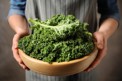 Photo of Woman holding fresh kale leaves on brown background, closeup