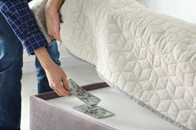Photo of Man hiding dollar banknotes under mattress in bedroom, closeup. Money savings