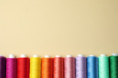 Photo of Set of colorful sewing threads on beige background, flat lay. Space for text