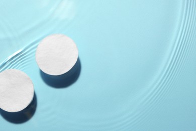 Image of Cotton pads in micellar water on light blue background, top view. Space for text