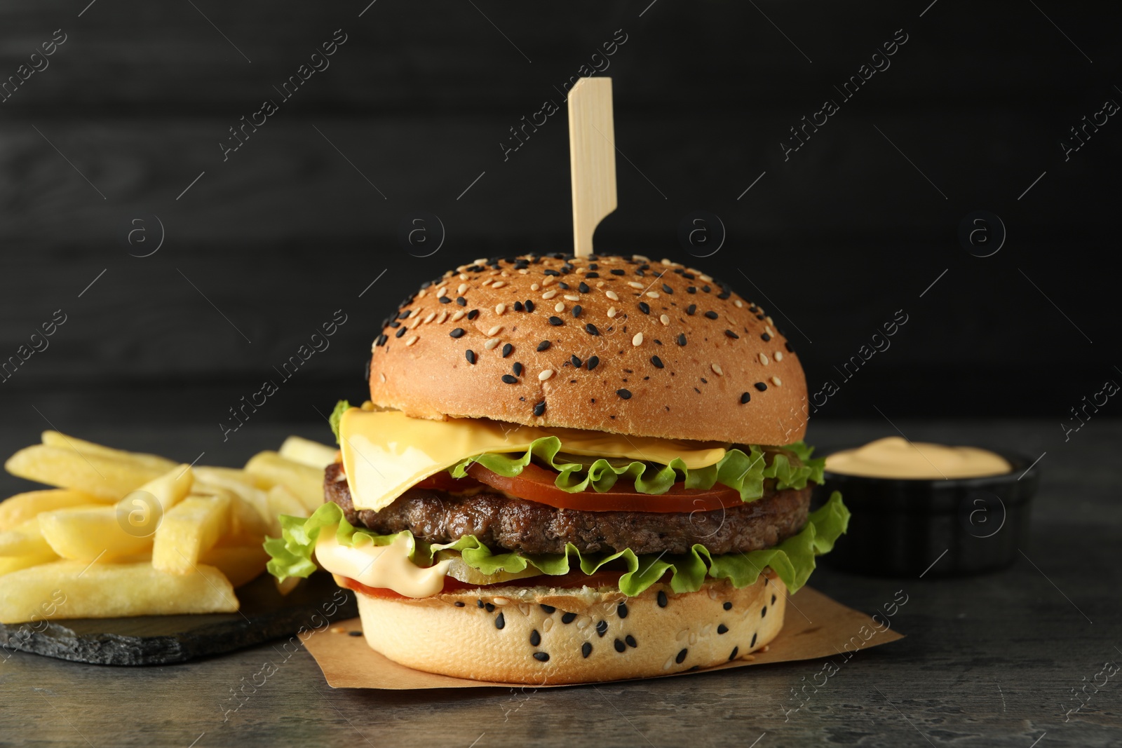 Burger with delicious patty, french fries and sauce on gray table against dark background Photo of Burger with delicious patty, french fries and sauce on gray table against dark background