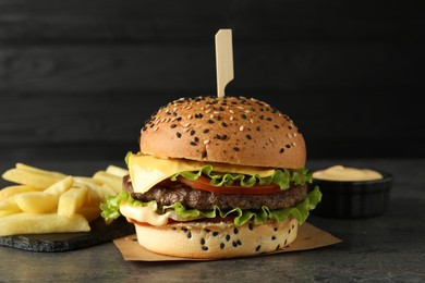 Photo of Burger with delicious patty, french fries and sauce on gray table against dark background