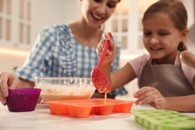 Mother and daughter making cupcakes together in kitchen, focus on ladle