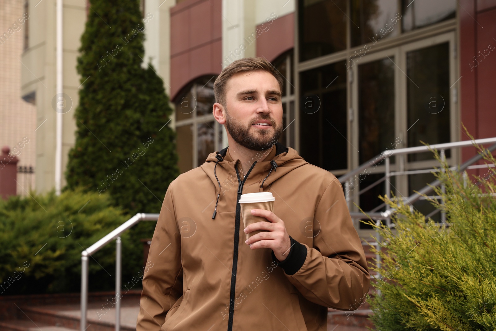 Photo of Handsome man wearing stylish clothes with cup of coffee on city street. Autumn walk