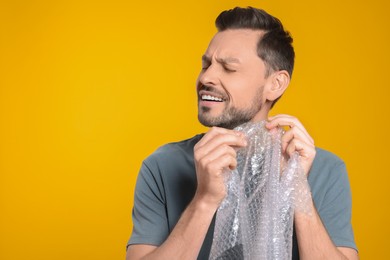 Photo of Man popping bubble wrap on yellow background, space for text. Stress relief