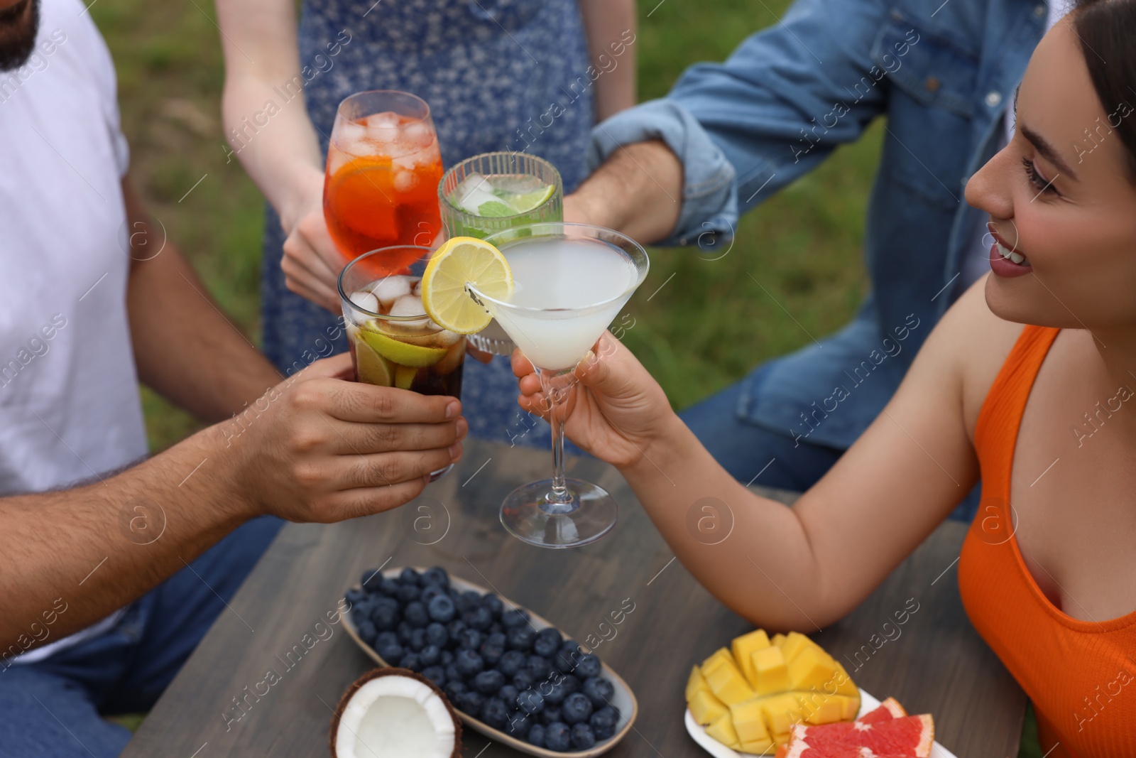 Photo of Friends clinking glasses with cocktails at table outdoors, closeup