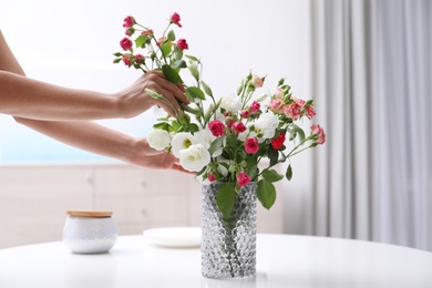 Photo of Woman taking beautiful flowers from vase on white table in room, closeup