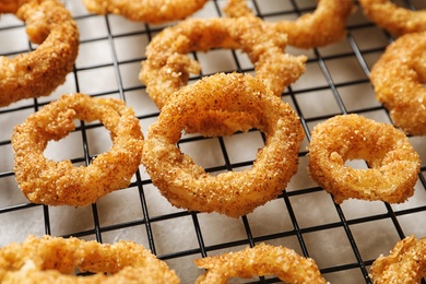 Photo of Cooling rack with homemade crunchy fried onion rings on table, closeup