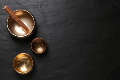 Photo of Golden singing bowls and mallet on black table, flat lay. Space for text