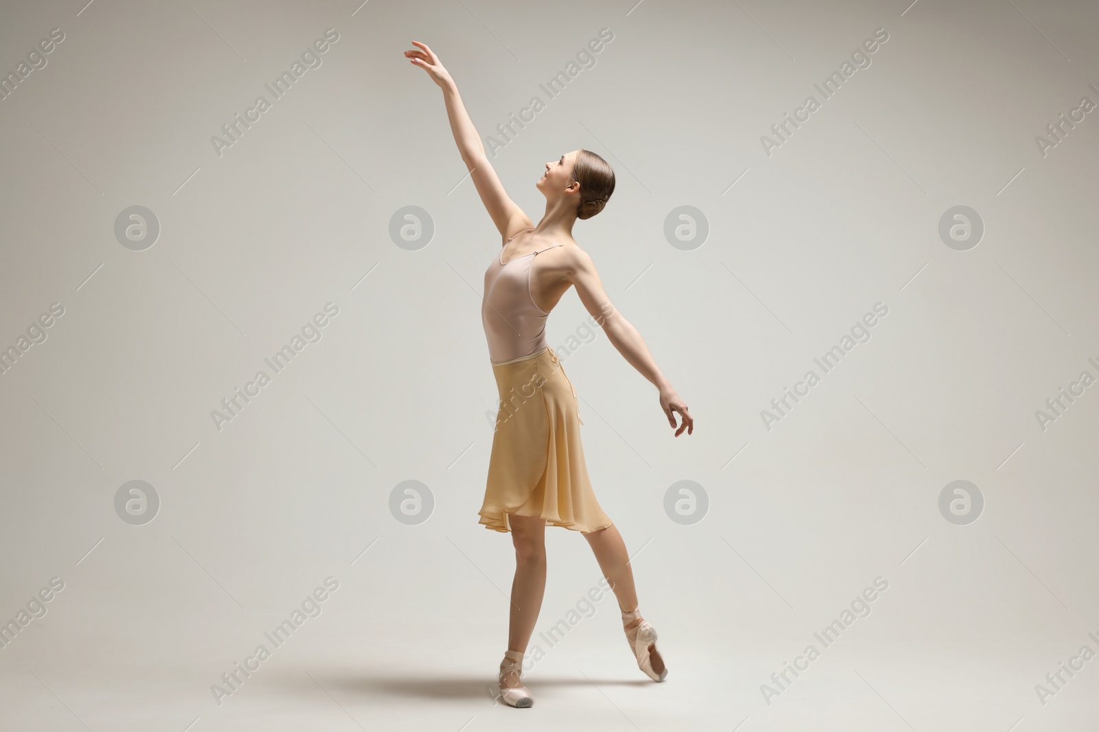 Photo of Young ballerina practicing dance moves on light grey background