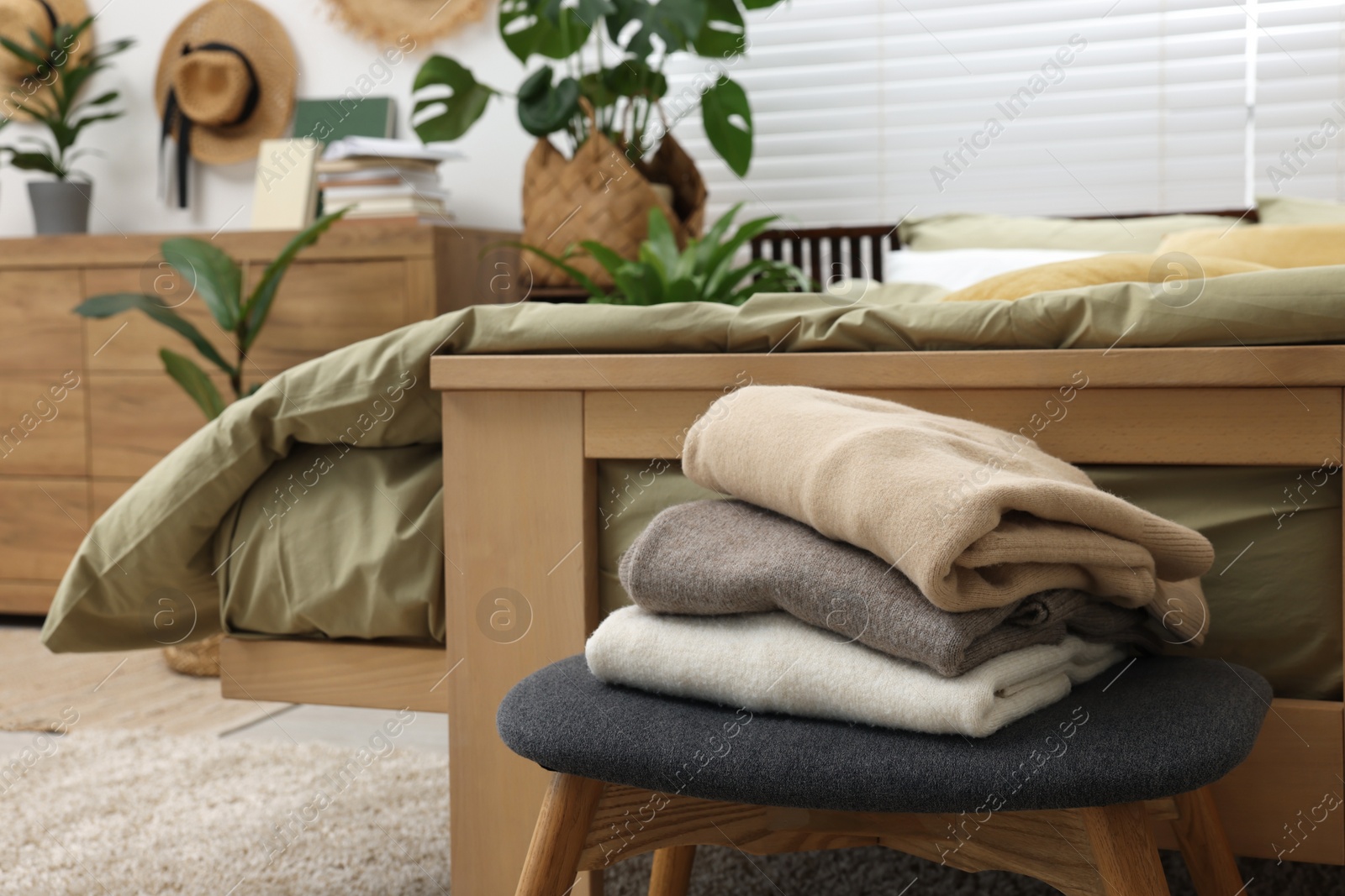 Photo of Clothes on ottoman, comfortable bed and houseplants in bedroom