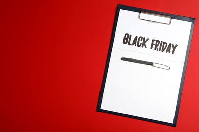 Photo of Clipboard with phrase Black Friday on red background, top view. Space for text