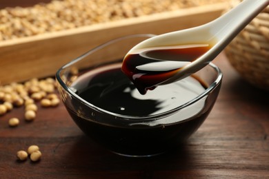 Photo of Taking soy sauce with spoon from bowl at wooden table, closeup