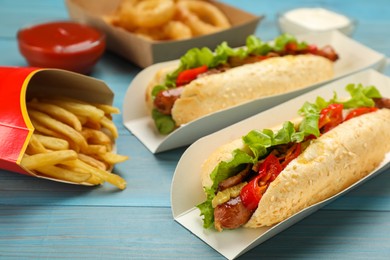 Tasty hot dogs and French fries served on light blue wooden table, closeup. Fast food