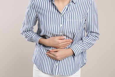 Photo of Woman suffering from stomach ache on beige background, closeup. Food poisoning