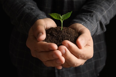 Man holding pile of soil and seedling, closeup