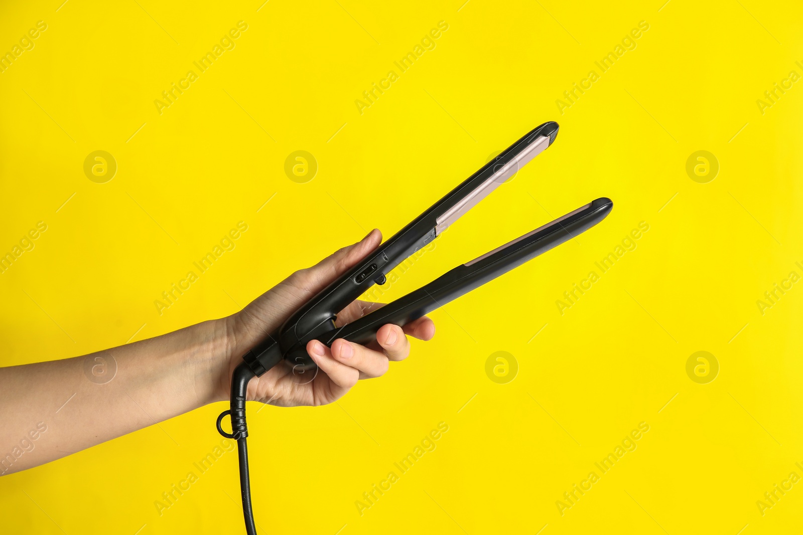 Photo of Woman holding flat hair iron on yellow background, closeup