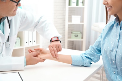 Doctor checking young woman's pulse with fingers in hospital, closeup