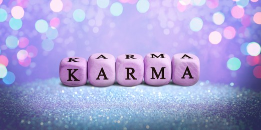 Image of Wooden cxubes with word Karma on shiny glitter against violet background. Banner design