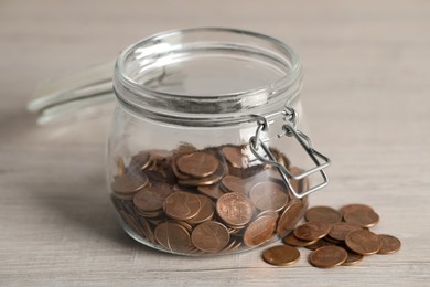 Glass jar with coins on white wooden table, closeup