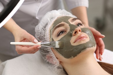 Photo of Cosmetologist applying mask on woman's face in clinic, closeup