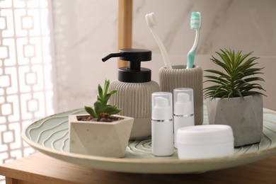 Photo of Holder with toothbrushes, different toiletries and plants on wooden table in bathroom, closeup