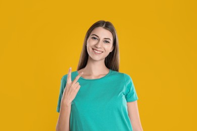 Woman showing number two with her hand on yellow background
