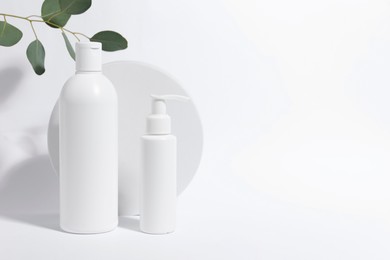 Photo of Bottles with cosmetic products and green leaves on white background, space for text. Stylish presentation