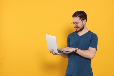 Photo of Happy man using laptop on orange background. Space for text