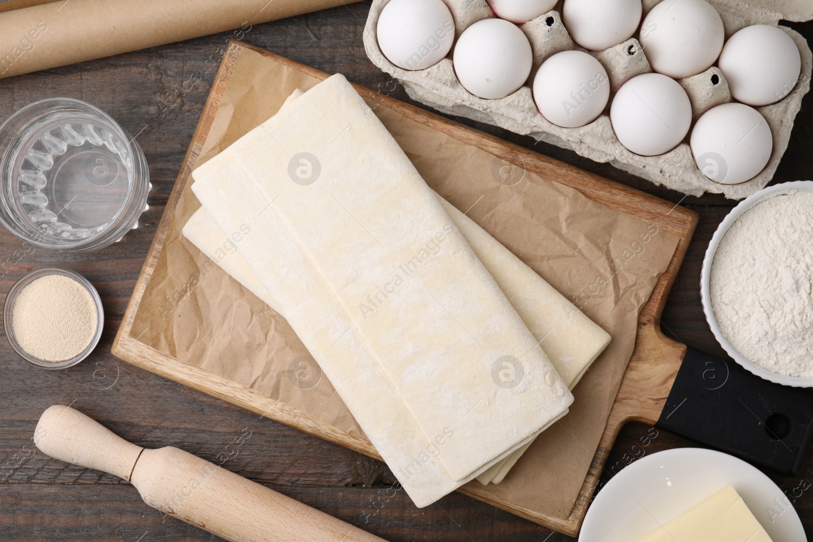 Photo of Raw puff pastry dough and ingredients on wooden table, flat lay