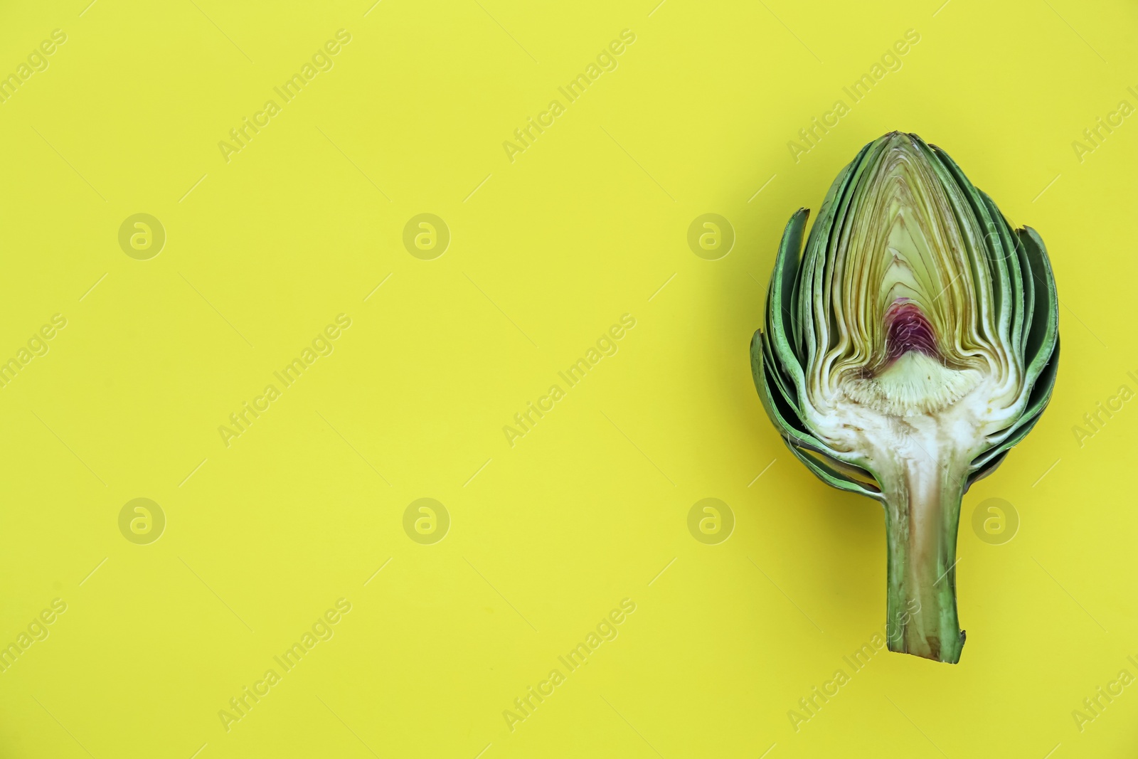 Photo of Cut fresh raw artichoke on yellow background, top view. Space for text