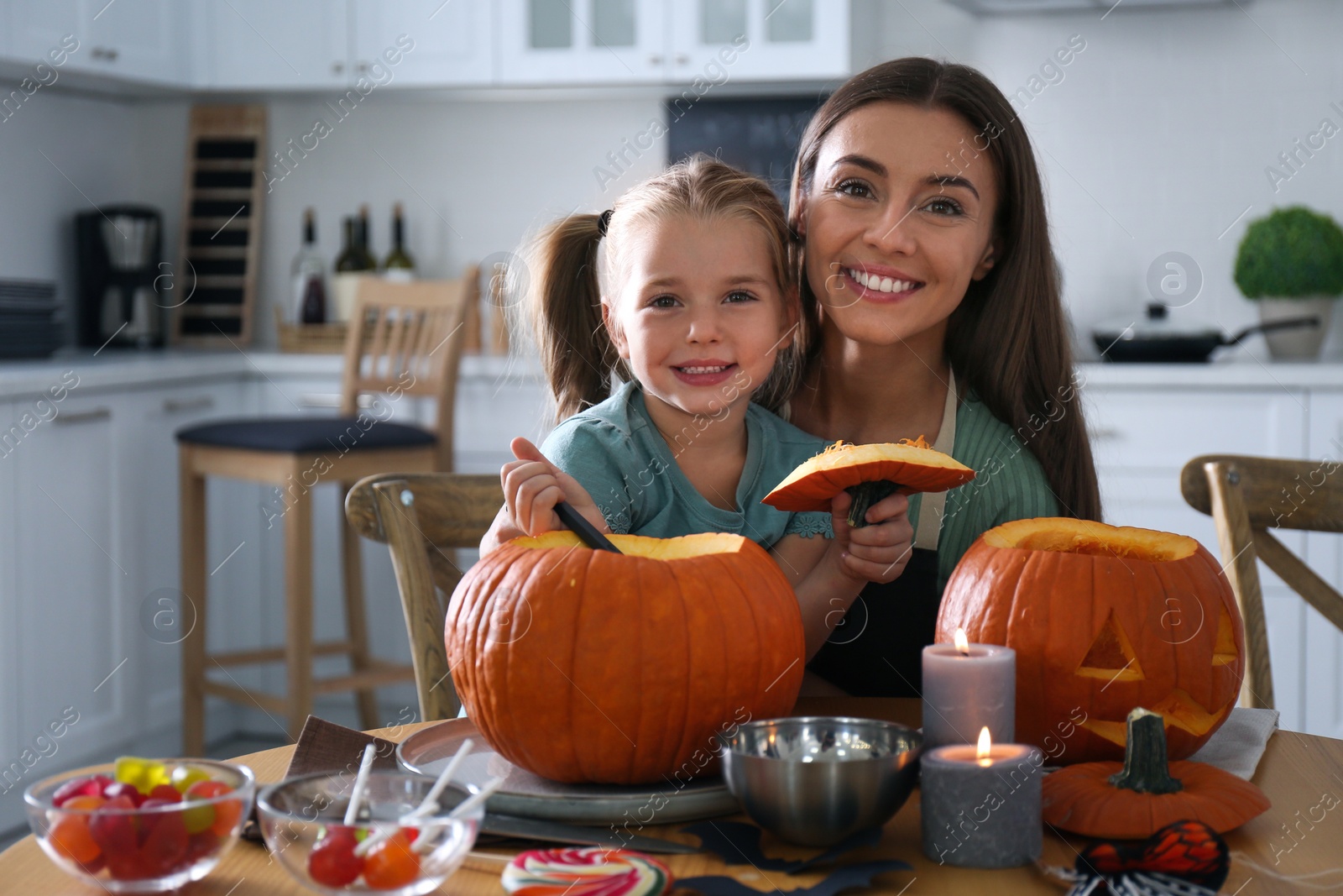 Photo of Mother and daughter making pumpkin jack o'lantern at table in kitchen. Halloween celebration