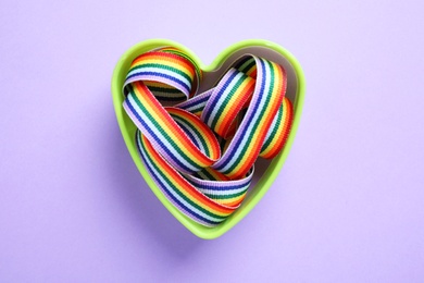 Photo of Heart shaped mold with bright rainbow ribbon on color background, top view. Symbol of gay community